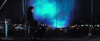 Movie still from “Grease” (1978), directed by Randal Kleiser – A man sitting on a bench in front of a light show; Wide shot, Low angle