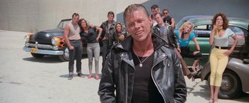 Movie still from “Grease” (1978), directed by Randal Kleiser – A man in a leather jacket standing in front of a group of people; Medium shot, Low angle