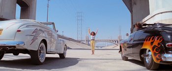 Movie still from “Grease” (1978), directed by Randal Kleiser – A woman jumping in the air in front of a car; Wide shot, Low angle