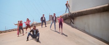 Movie still from “Grease” (1978), directed by Randal Kleiser – A group of people standing on top of a cement wall; Wide shot, Overhead angle