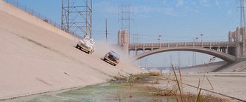Movie still from “Grease” (1978), directed by Randal Kleiser – A couple of cars driving down a dirt road; Extreme Wide shot, High angle