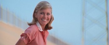 Movie still from “Grease” (1978), directed by Randal Kleiser – A woman in a pink shirt smiling for the camera; Close Up shot, Low angle
