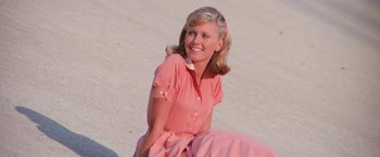 Movie still from “Grease” (1978), directed by Randal Kleiser – A woman in a pink dress sitting on the ground; Medium shot, Low angle