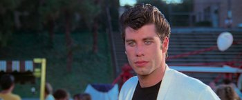 Movie still from “Grease” (1978), directed by Randal Kleiser – A young man in a black t - shirt and a white jacket; Close Up shot, Over the shoulder angle