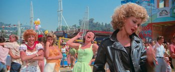 Movie still from “Grease” (1978), directed by Randal Kleiser – A group of people standing around at an amusement park; Medium shot, Over the shoulder angle