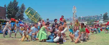 Movie still from “Grease” (1978), directed by Randal Kleiser – A group of people sitting on the ground at a carnival; Extreme Wide shot, High angle