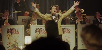 Movie still from “Green Book” (2018), directed by Peter Farrelly – A man standing in front of an orchestra with his hands raised; Medium shot, Low angle