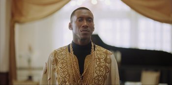 Movie still from “Green Book” (2018), directed by Peter Farrelly – A man in a gold and black outfit standing in front of a piano; Close Up shot, Low angle