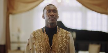 Movie still from “Green Book” (2018), directed by Peter Farrelly – A man in a gold and black outfit standing in front of a piano; Close Up shot, Low angle