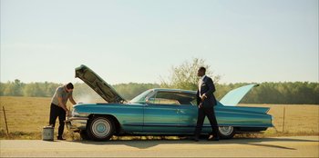 Movie still from “Green Book” (2018), directed by Peter Farrelly – A man standing next to an old blue car with the hood open; Wide shot, Low angle