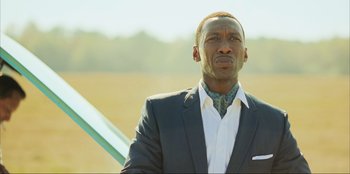 Movie still from “Green Book” (2018), directed by Peter Farrelly – A man wearing a suit and tie standing in front of a fence; Close Up shot, Low angle