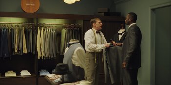 Movie still from “Green Book” (2018), directed by Peter Farrelly – A man in a suit and tie talking to another man in a suit and tie in a suit shop; Medium shot, Over the shoulder angle