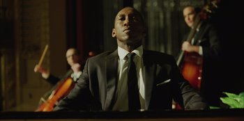 Movie still from “Green Book” (2018), directed by Peter Farrelly – A man wearing a suit and tie sitting in front of a microphone; Close Up shot, Low angle