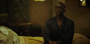 Movie still from “Green Book” (2018), directed by Peter Farrelly – A man sitting on top of a bed in a room; Medium shot, Over the shoulder angle