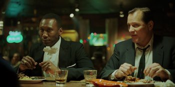 Movie still from “Green Book” (2018), directed by Peter Farrelly – Two men sitting at a dinner table with drinks; Medium shot, Over the shoulder angle