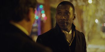 Movie still from “Green Book” (2018), directed by Peter Farrelly – A man in a black jacket is standing in front of some lights; Close Up shot, Over the shoulder angle