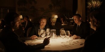 Movie still from “Another Round” (2020), directed by Thomas Vinterberg – A group of people sitting at a table with wine glasses on it; Medium shot, Over the shoulder angle