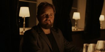 Movie still from “Another Round” (2020), directed by Thomas Vinterberg – A man with a goatee sitting in front of two lamps; Close Up shot, Over the shoulder angle