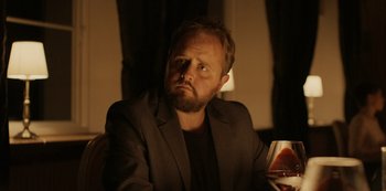Movie still from “Another Round” (2020), directed by Thomas Vinterberg – A man sitting at a table with a glass of red wine; Close Up shot, Over the shoulder angle