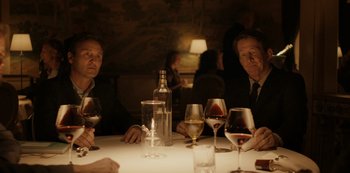 Movie still from “Another Round” (2020), directed by Thomas Vinterberg – Two men sitting at a dinner table with wine glasses; Medium shot, Over the shoulder angle