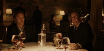 Movie still from “Another Round” (2020), directed by Thomas Vinterberg – A man sitting at a table with a glass of wine; Medium shot, Over the shoulder angle
