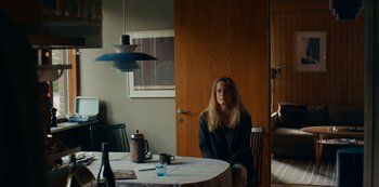Movie still from “Another Round” (2020), directed by Thomas Vinterberg – A woman sitting at a dining room table in front of a wine bottle; Medium shot, Low angle
