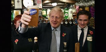 Movie still from “Another Round” (2020), directed by Thomas Vinterberg – A man in a suit and tie holding up a glass of beer; Medium shot, Low angle
