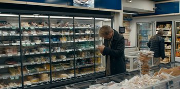 Movie still from “Another Round” (2020), directed by Thomas Vinterberg – A man standing in front of a display case in a grocery store; Medium shot, Over the shoulder angle