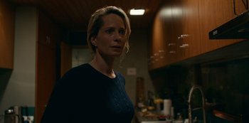 Movie still from “Another Round” (2020), directed by Thomas Vinterberg – A woman standing in a dark kitchen looking to her left; Medium shot, Low angle