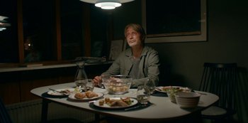 Movie still from “Another Round” (2020), directed by Thomas Vinterberg – A man sitting at a table with plates of food; Medium shot, Low angle