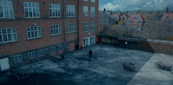 Movie still from “Another Round” (2020), directed by Thomas Vinterberg – A person standing in a parking lot next to a building; Extreme Wide shot, High angle