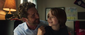 Movie still from “Greenland” (2020), directed by Ric Roman Waugh – A man and a boy smiling for the camera; Close Up shot, Over the shoulder angle