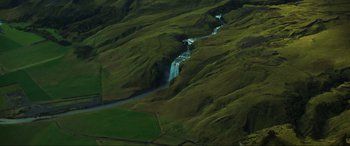Movie still from “Greenland” (2020), directed by Ric Roman Waugh – A view from above of a waterfall on a lush green hillside; Extreme Wide shot, High angle