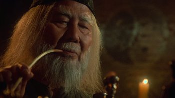 Movie still from “Gremlins” (1984), directed by Joe Dante – An old man with a long white beard smoking a pipe; Close Up shot, Low angle