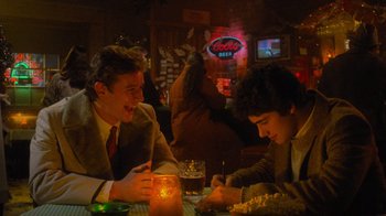 Movie still from “Gremlins” (1984), directed by Joe Dante – Two men sitting at a table in front of drinks; Medium shot, Over the shoulder angle