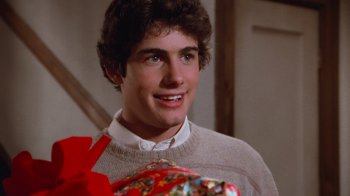 Movie still from “Gremlins” (1984), directed by Joe Dante – A young man holding a present in a room; Close Up shot, Over the shoulder angle