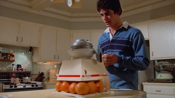 Movie still from “Gremlins” (1984), directed by Joe Dante – A young man in a blue shirt and a box of oranges; Medium shot, Low angle