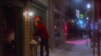 Movie still from “Gremlins” (1984), directed by Joe Dante – A man in a red jacket standing in front of a store; Wide shot, High angle