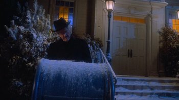 Movie still from “Gremlins” (1984), directed by Joe Dante – An older man in a black jacket and a black hat is sitting in front of a mailbox; Medium shot, Low angle