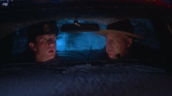 Movie still from “Gremlins” (1984), directed by Joe Dante – Two police officers in the back of a police car at night; Close Up shot, Low angle