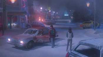 Movie still from “Gremlins” (1984), directed by Joe Dante – Two people standing on the side of the road near a car; Wide shot, High angle