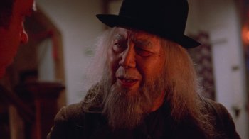 Movie still from “Gremlins” (1984), directed by Joe Dante – An old man with long white beard wearing a black hat; Close Up shot, Over the shoulder angle