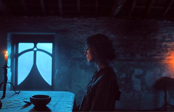 Movie still from “Gretel & Hansel” (2020), directed by Oz Perkins – A woman sitting at a table in front of a window; Medium shot, Over the shoulder angle