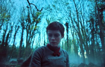Movie still from “Gretel & Hansel” (2020), directed by Oz Perkins – A young man with a red bow tie standing in front of trees; Medium shot, Low angle