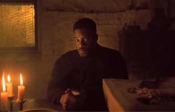 Movie still from “Gretel & Hansel” (2020), directed by Oz Perkins – A man sitting at a table in a dark room; Medium shot, High angle