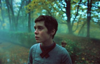 Movie still from “Gretel & Hansel” (2020), directed by Oz Perkins – A young boy in a red bow tie in the woods; Close Up shot, Over the shoulder angle