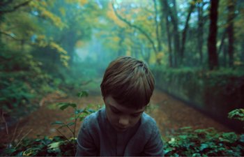 Movie still from “Gretel & Hansel” (2020), directed by Oz Perkins – A young boy sitting in the middle of a forest; Medium shot, High angle