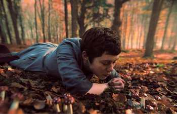 Movie still from “Gretel & Hansel” (2020), directed by Oz Perkins – A boy laying on the ground in the woods; Medium shot, Low angle