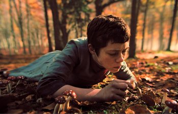 Movie still from “Gretel & Hansel” (2020), directed by Oz Perkins – A young boy laying on the ground in the woods; Close Up shot, High angle