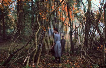 Movie still from “Gretel & Hansel” (2020), directed by Oz Perkins – Two people standing in the woods near a fence; Wide shot, High angle